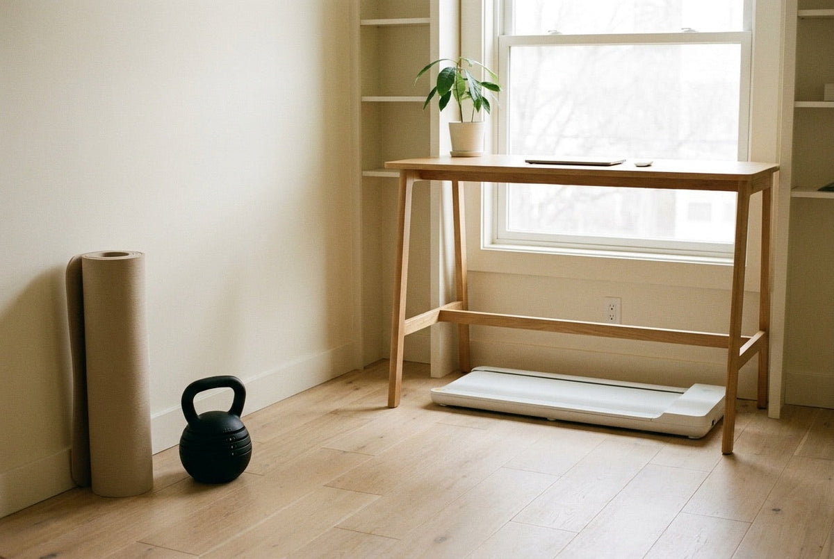 Walking pad under a standing desk with a kettlebell and a rolled mat